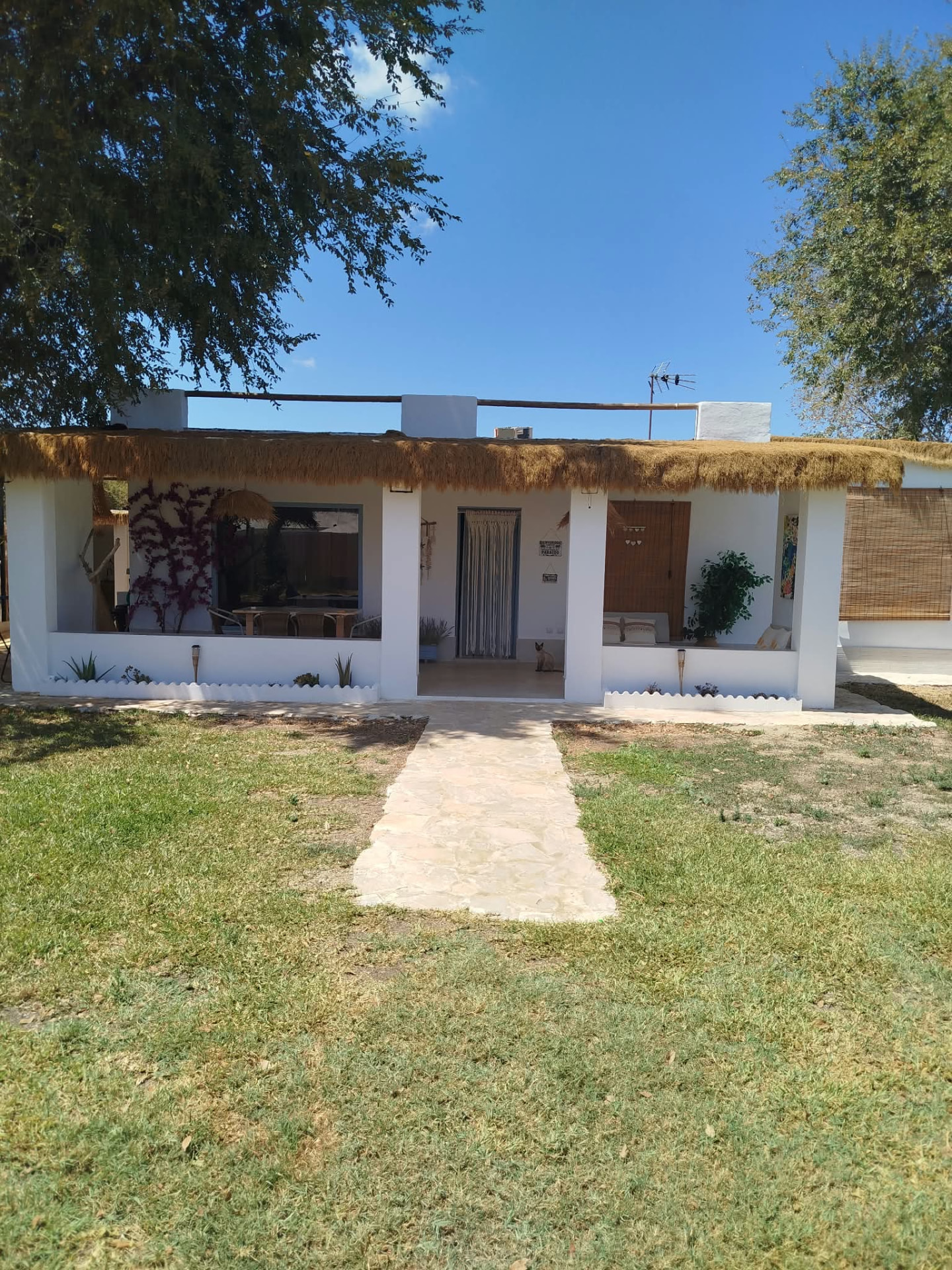 Fachada encalada de la casa rural con porche de brezo y jardín